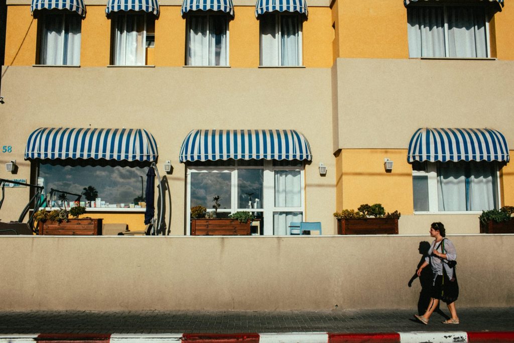 woman walking down a sidewalk in front of a building with blue and white striped awnings